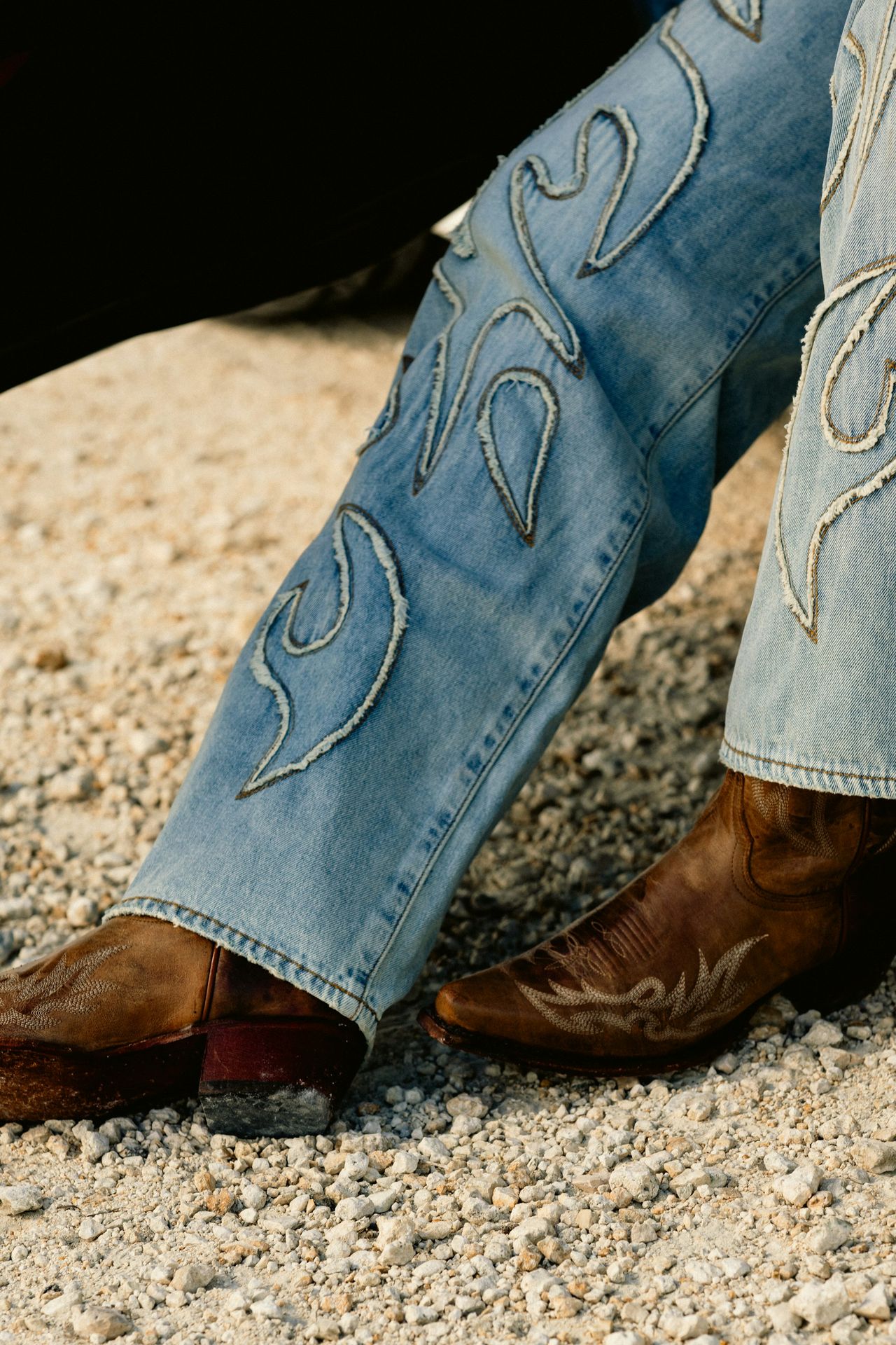 A person wearing cowboy boots sitting on the ground